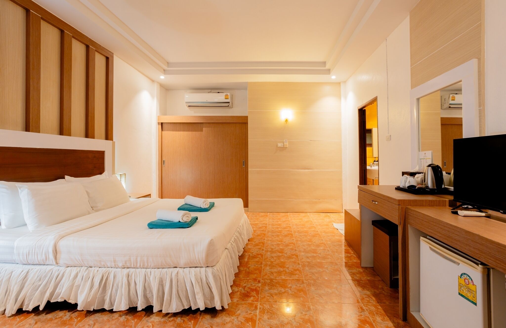 Una habitación de hotel con cama, escritorio con televisor y equipo de aire acondicionado.