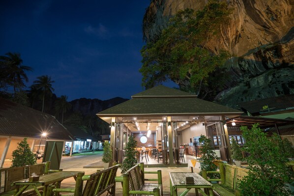 An outdoor seating area with tables and chairs, a covered pavilion, and a view of a mountainous landscape. - Tonsai Bay Resort (Krabi)