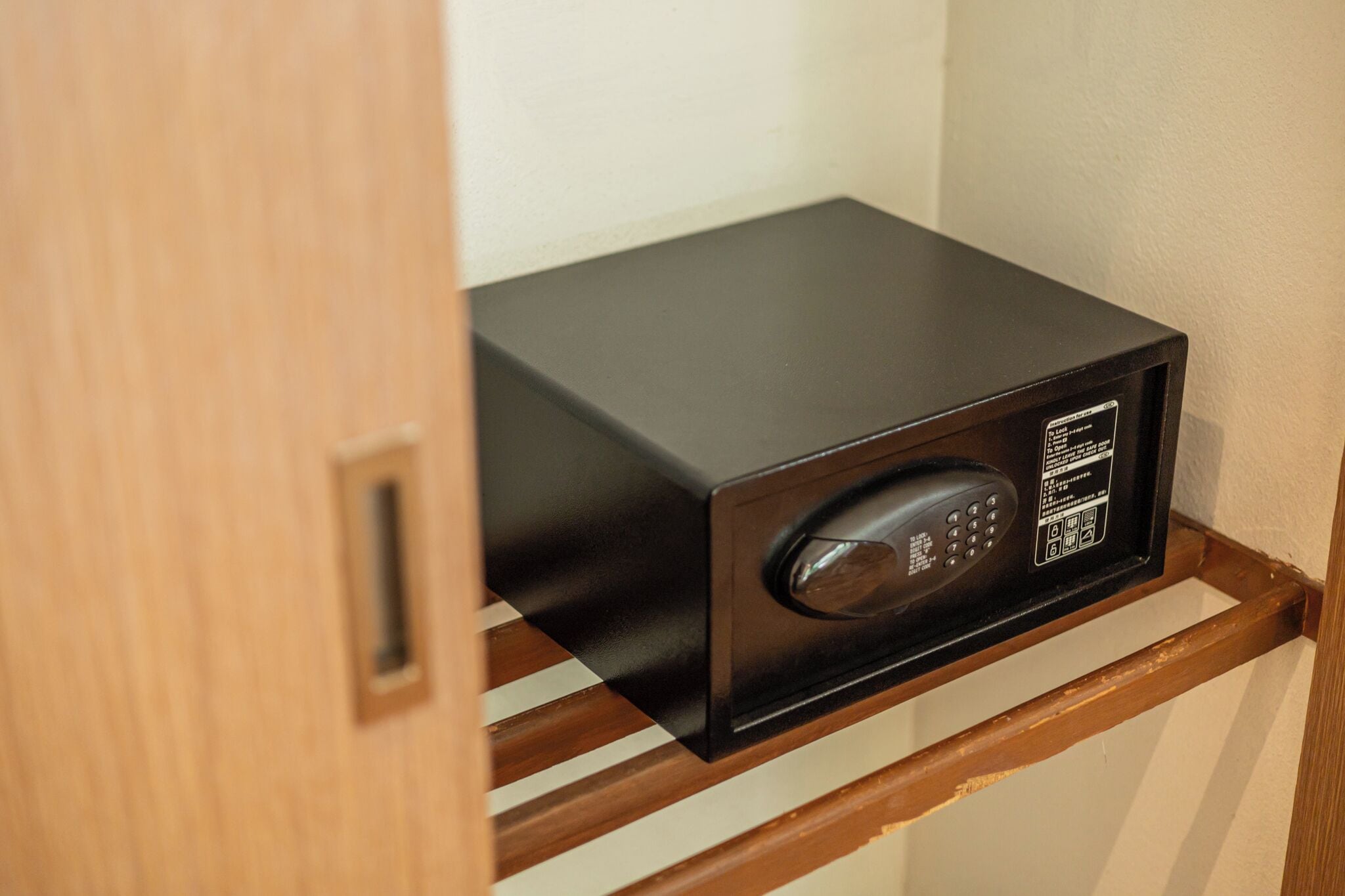 A black microwave on a wooden shelf in a room with a wooden door.
