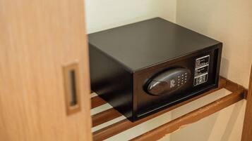 A black microwave on a wooden shelf in a room with a wooden door.