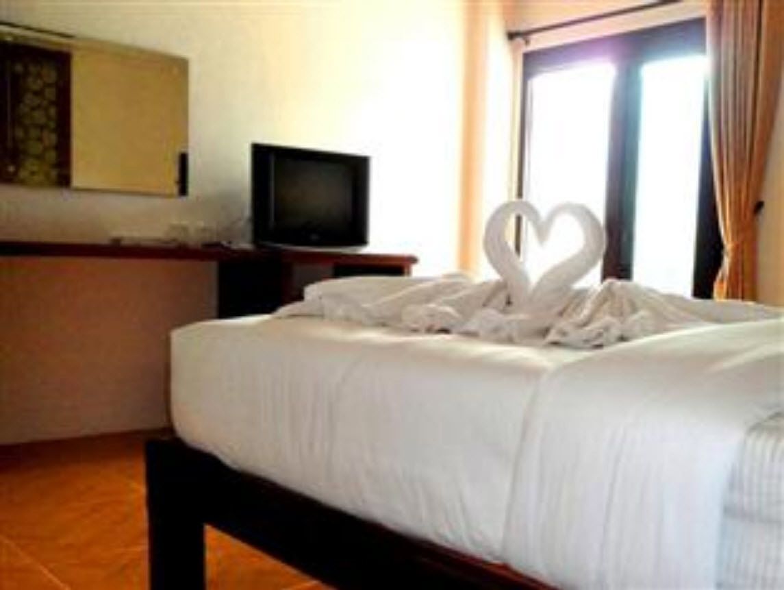 Una habitació d'hotel amb un llit, una televisió sobre un suport i una tovallola amb forma de cor sobre el llit.