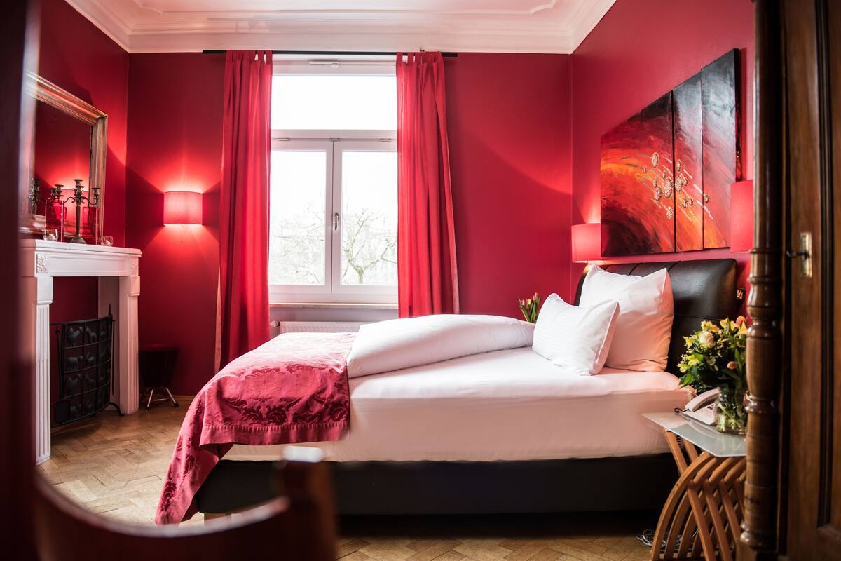 Una camera da letto con un letto, un comodino, uno specchio, un camino e una finestra con tende.