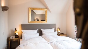 Una cama bien hecha con sábanas blancas, cabecera de madera y lámparas de noche.