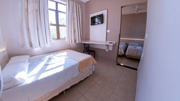 A bedroom with a bed, a desk, a chair, a TV, and a mirror.