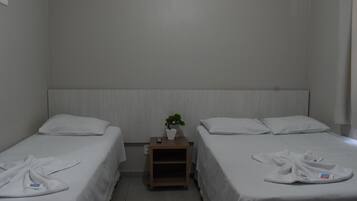 A hotel room with two single beds, a small wooden nightstand with a plant, and a white towel on each bed.