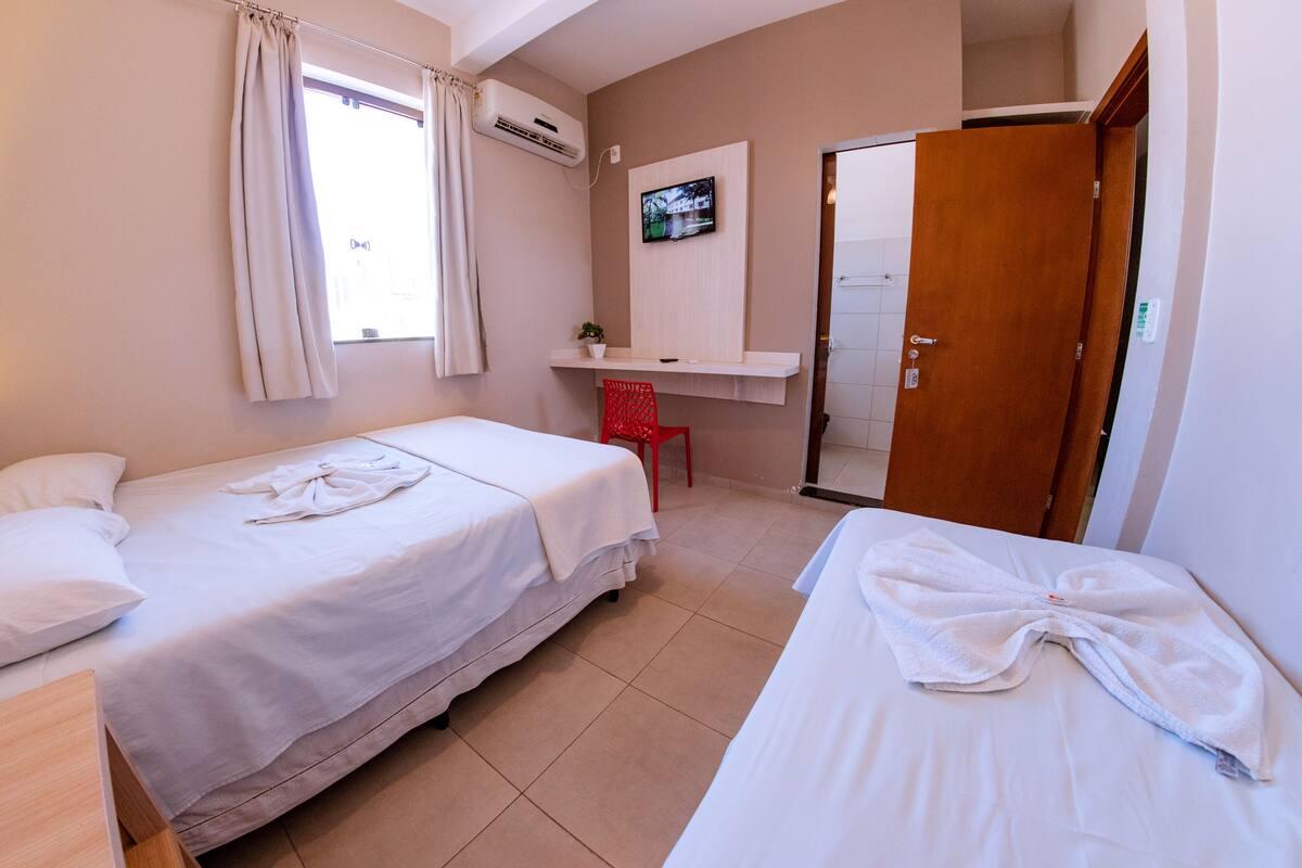 Habitación de hotel con dos camas, un televisor en la pared, un escritorio pequeño y una puerta corredera.