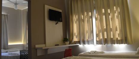 A hotel room with two beds, a TV mounted on the wall, a ceiling fan, and a window with curtains.