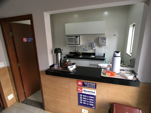 A hotel reception area with a counter, a coffee machine, a microwave, and a sign indicating room numbers. - Hotel Ipiranga (Maringá)