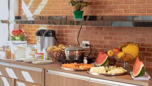A breakfast buffet with various food items and a brick wall in the background. - Hotel Ipiranga (Maringá)