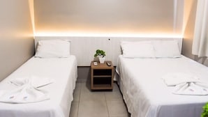 A hotel room with two single beds, a bedside table with a plant, and a wall-mounted light fixture. - Hotel Ipiranga (Maringá)