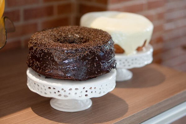 A chocolate donut on a white cake stand. - Hotel Ipiranga (Maringá)