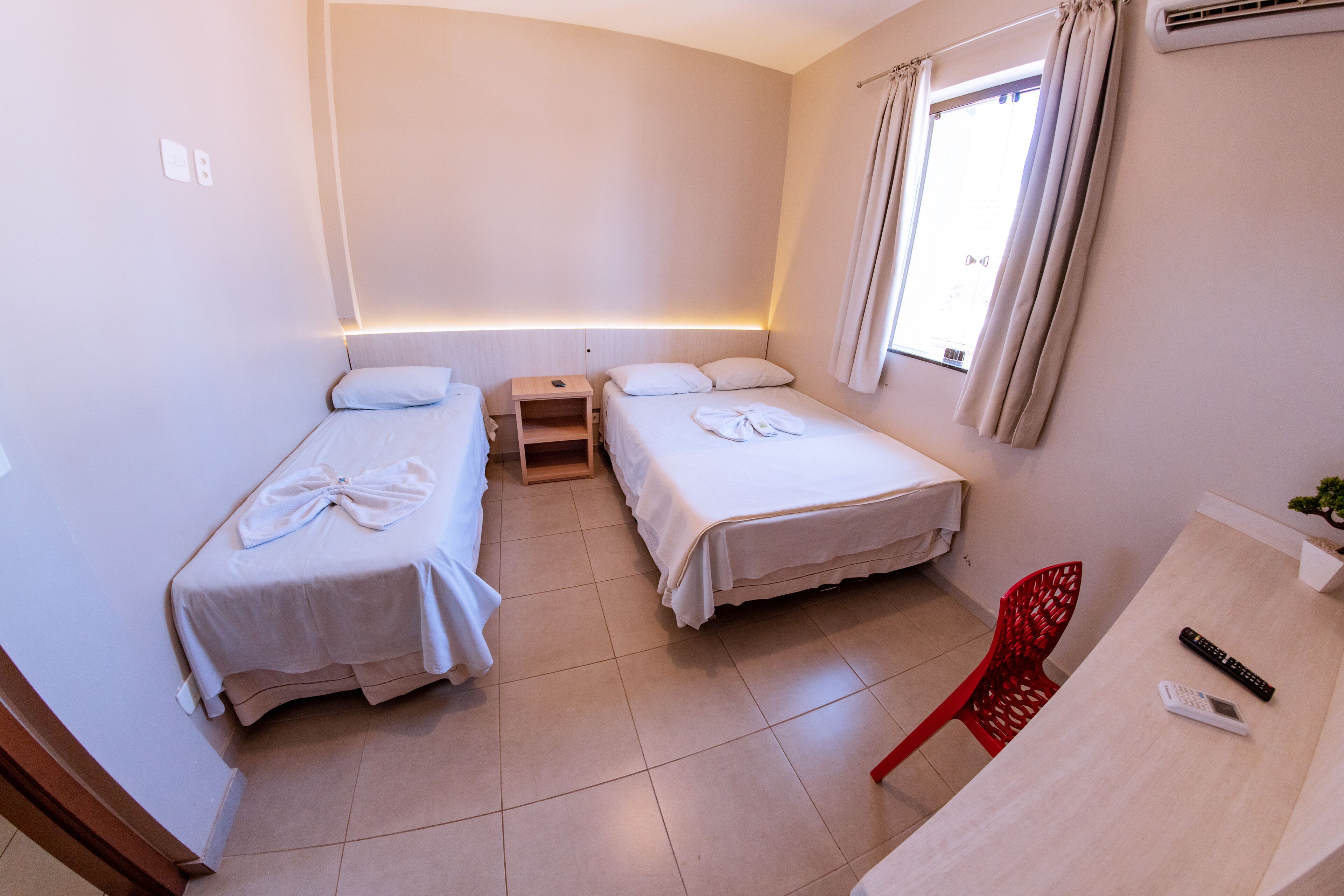 A small, clean room with two beds, a desk, and a chair.