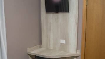 A room with a bed, a desk with a chair, a mounted TV, and an air conditioning unit.