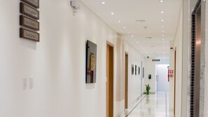 A long, well-lit hallway with white walls, a tiled floor, and several doors. - Roari Hotel (Cuiabá)