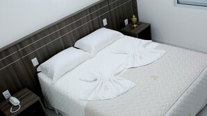 A neatly made bed with white linens and towels arranged on the bed. There are two bedside tables with a telephone and a lamp on each. - Roari Hotel (Cuiabá)