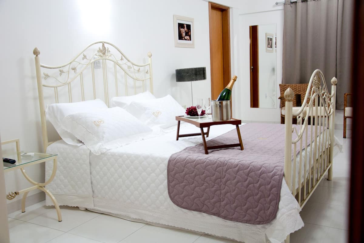 A neatly made bed with a white headboard, a bedside table with a glass top, and a purple throw blanket.
