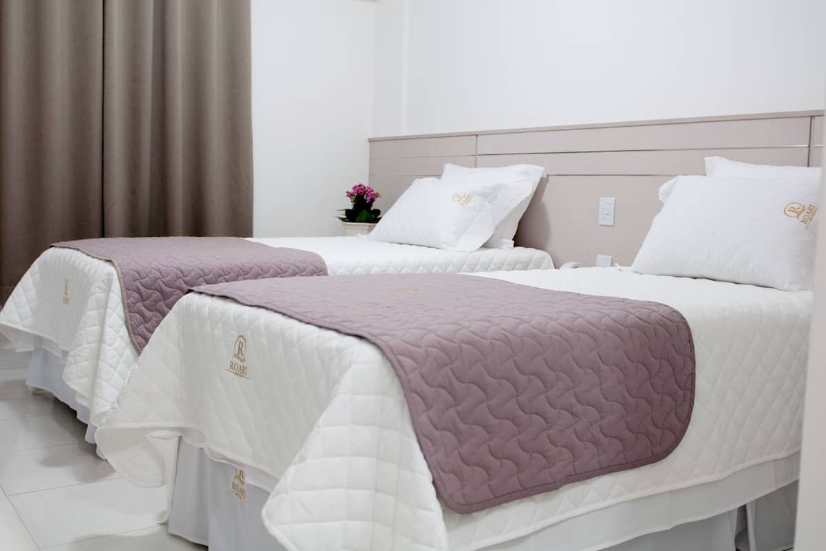 A hotel room with two beds, each with a white quilted bedspread and a purple blanket.