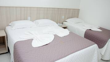 A hotel room with two beds, each with a white comforter and a pink quilted bedspread. There is a wooden headboard, a bedside table with a phone, and a nightstand with a lamp.