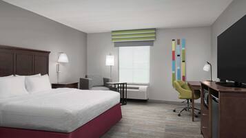 A hotel room with a large bed, a desk, a chair, a television, and a window with blinds.
