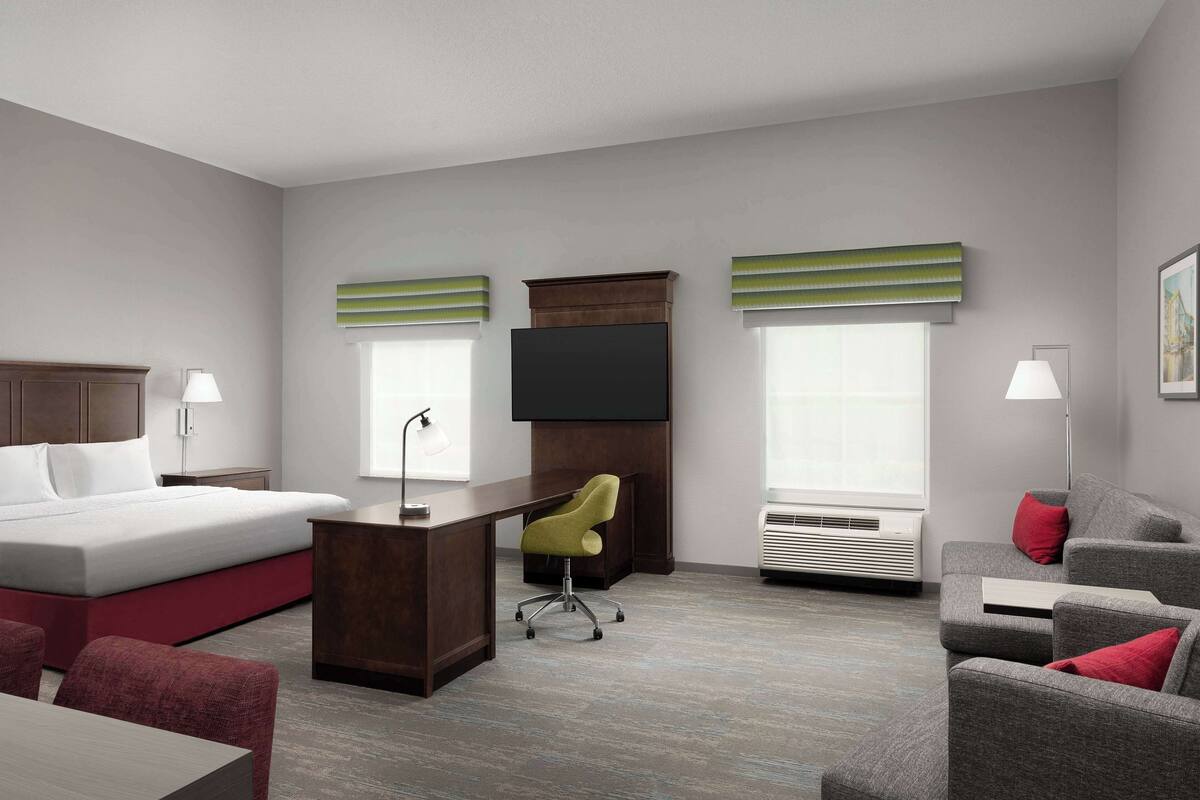 A hotel room with a bed, desk, chair, and a TV.