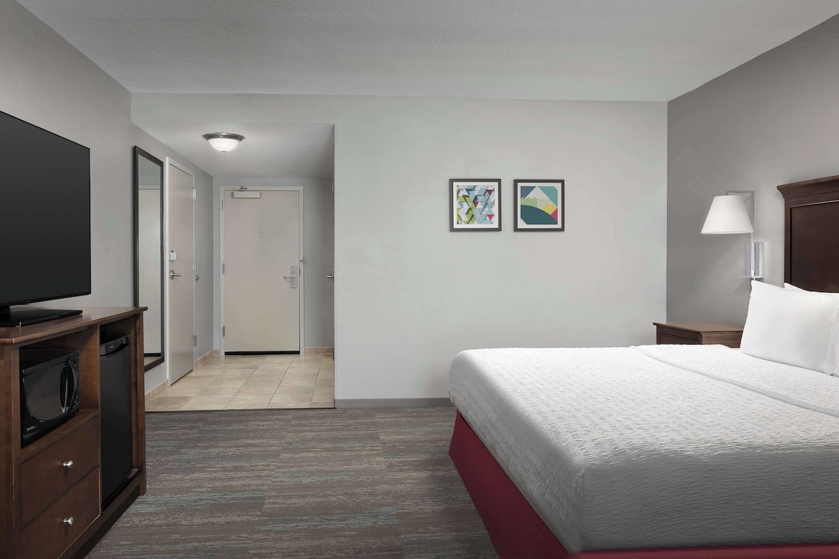 A hotel room with a bed, a television, a desk, and a door leading to a bathroom.