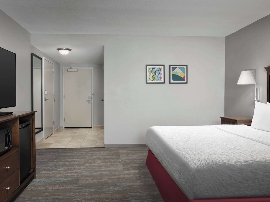 A hotel room with a bed, a television, a desk, and a door leading to a bathroom.