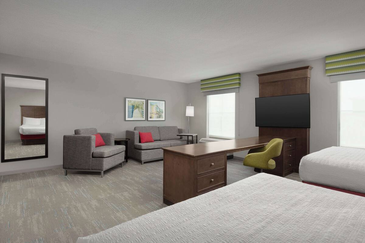 A hotel room with a bed, a desk, a sofa, a chair, a TV, a dresser, and a mirror.