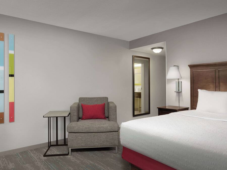 Una camera d'albergo con un letto, una sedia, un tavolino, una lampada e uno specchio.