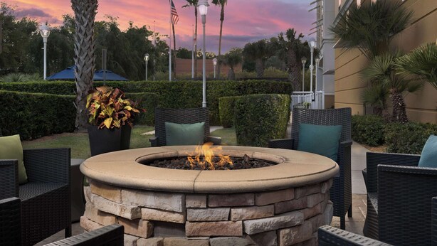 A circular stone fire pit with flames, surrounded by wicker chairs and a potted plant.