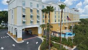 A hotel with a pool, palm trees, and a clear sky.