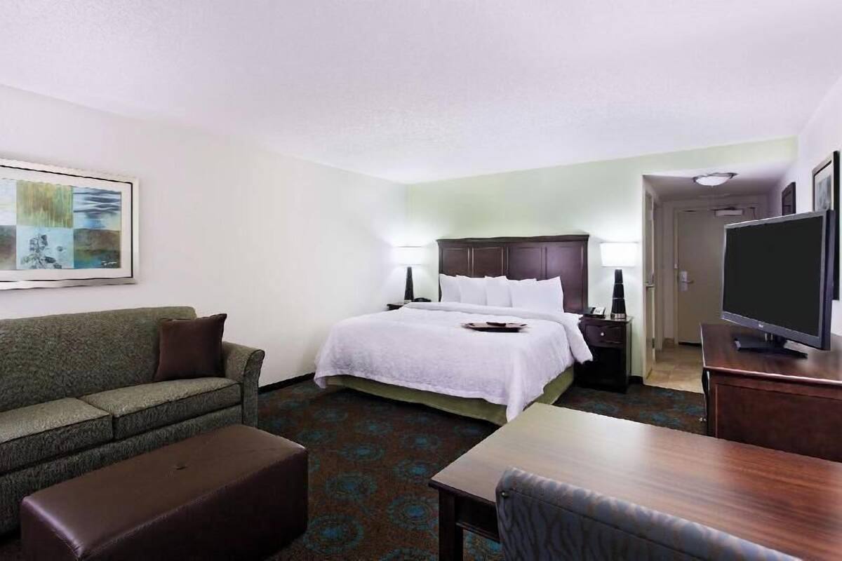 A hotel room with a bed, a sofa, a desk, a television, and a painting on the wall.