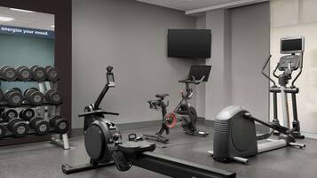 Ein Fitnessraum mit Cardiogeräten, Kurzhanteln und einem Fernseher.
