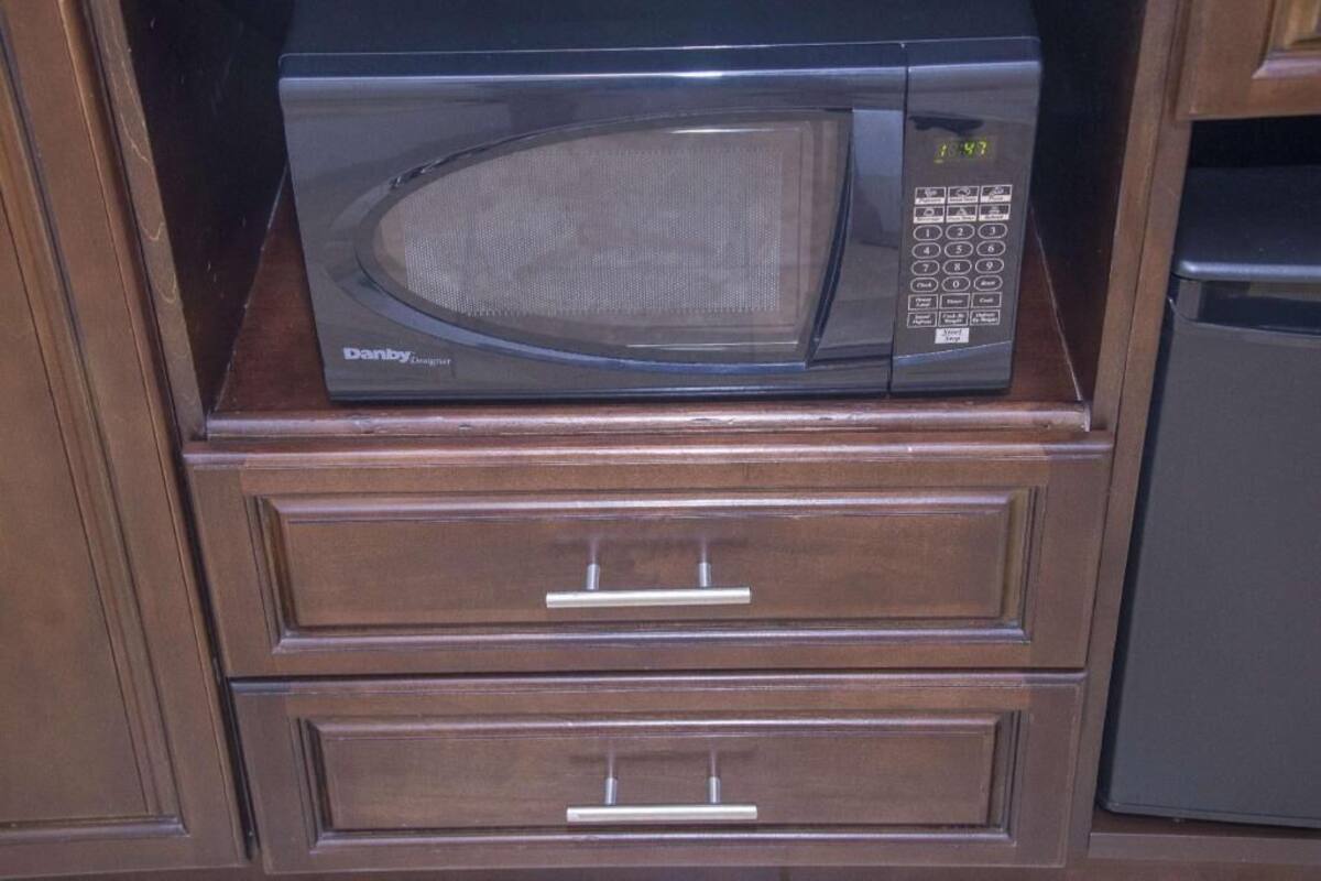 A microwave oven on a wooden cabinet shelf.