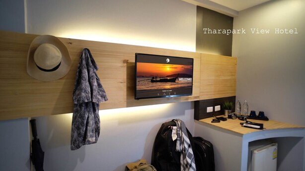 A hotel room with a mounted TV displaying a sunset view, a hat, a jacket, and a desk with a camera and other items. - Tharapark View Hotel (Krabi)