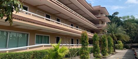Um hotel com vários andares, varandas, área de estacionamento e áreas verdes ajardinadas.