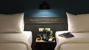A room with two beds, a nightstand with a lamp, a plant, a bottle, and a book. - Tharapark View Hotel (Krabi)