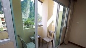 A balcony with a chair and a small table, a sliding glass door, and a view of greenery outside. - Pranang Flora House (Krabi)