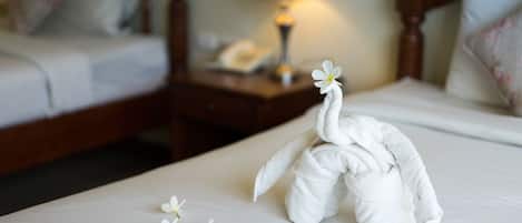 Una cama bien hecha con una escultura de toalla con forma de cisne, rodeada de flores blancas.