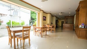 A spacious dining area with wooden tables and chairs, a kitchen area with wooden cabinets, and a view of greenery outside. - Pranang Flora House (Krabi)