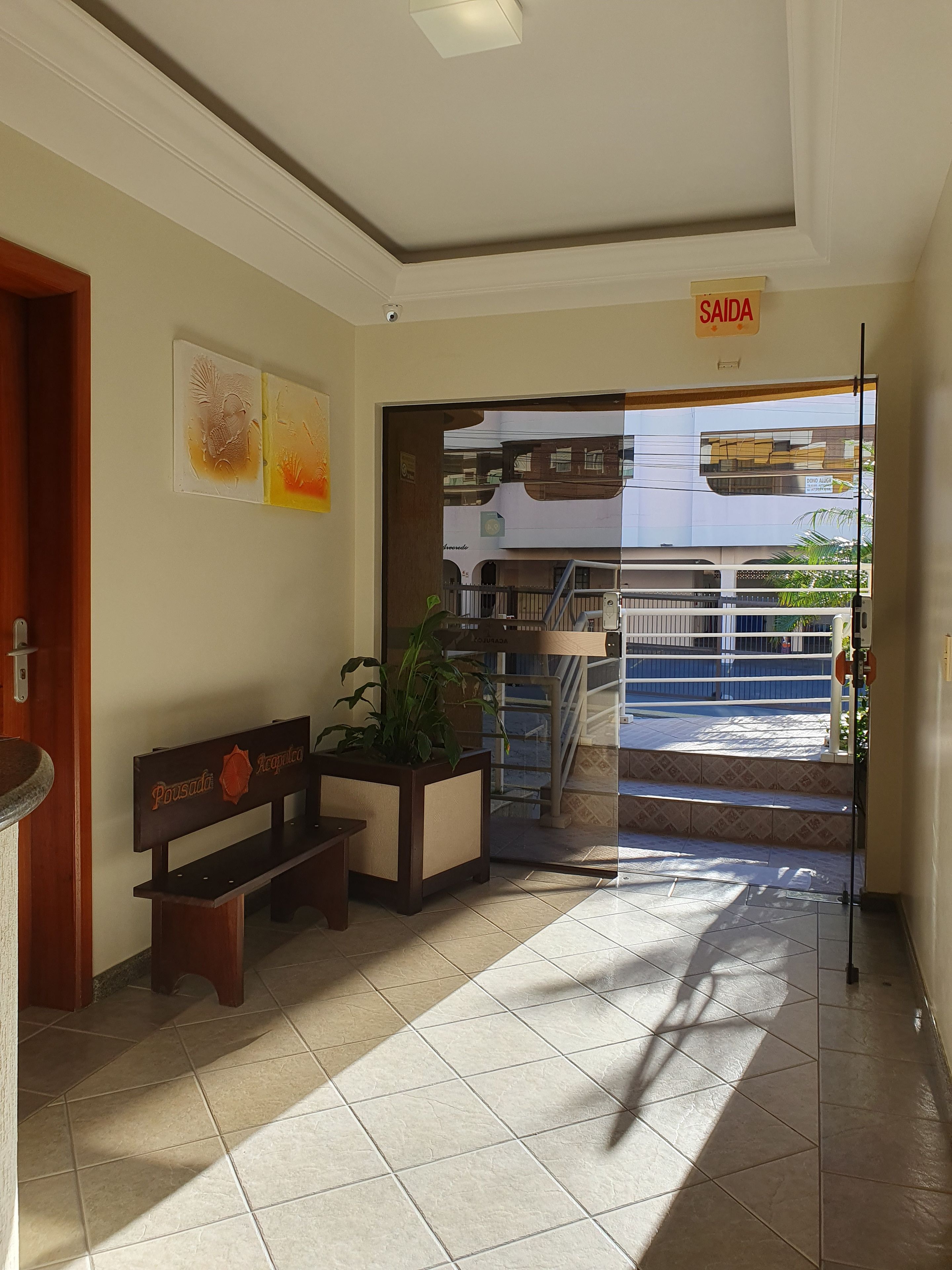 A hotel lobby with a bench, a potted plant, and a sign indicating the exit.