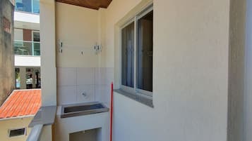 A small bathroom with a sink, a window, and a broom leaning against the wall.