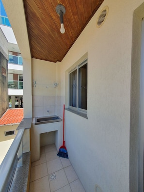 Un baño pequeño con lavamanos, ventana y una escoba apoyada en la pared.