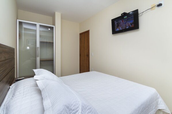A bedroom with a bed, a wardrobe, and a TV mounted on the wall. - Acapulco - Apartamentos (Bombinhas)