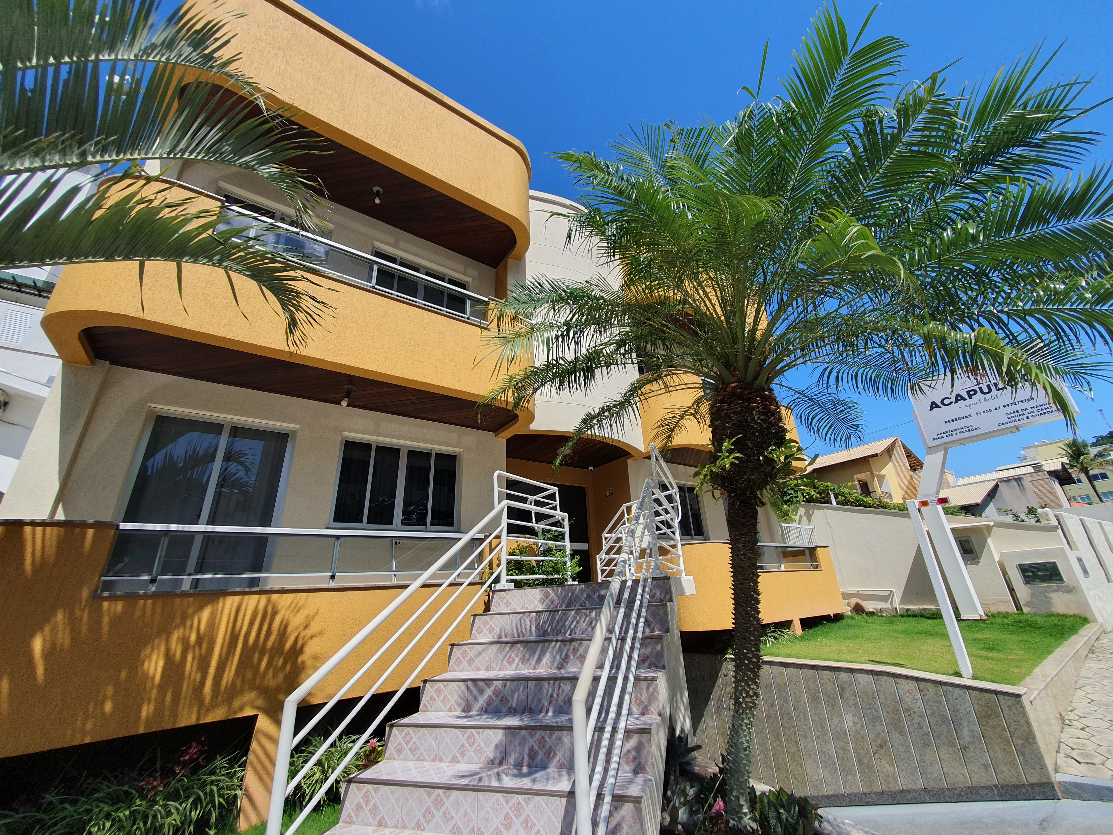 A multi-story hotel with a yellow facade, a palm tree, and a signboard.