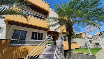 A multi-story hotel with a yellow facade, a palm tree, and a signboard.
