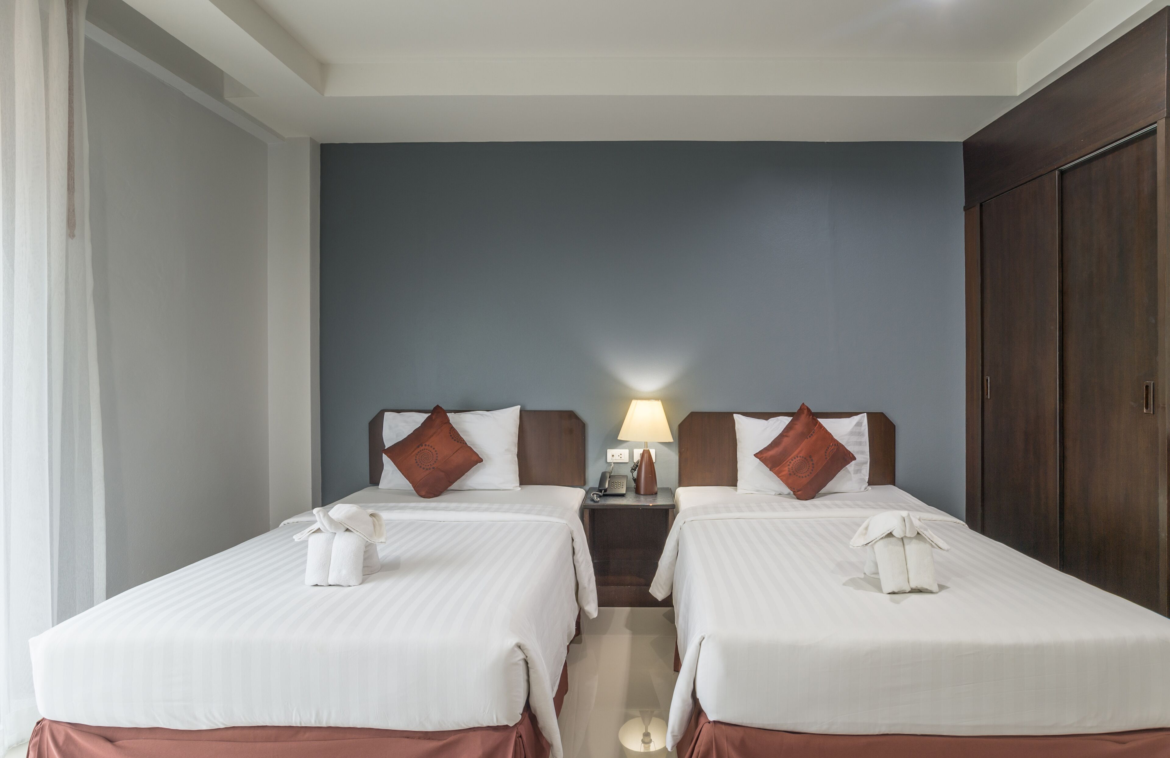 A hotel room with two beds, a nightstand with a lamp, and a wardrobe.
