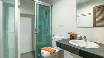 Un baño moderno con cabina de ducha de vidrio, inodoro blanco, lavabo con espejo y un pequeño jarrón con flores sobre la encimera.