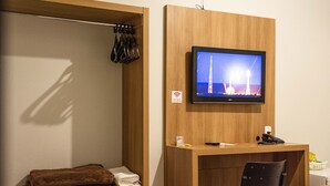 Camera d'albergo con una scrivania in legno, una televisione a parete, un letto, una sedia e uno scaffale con asciugamani.