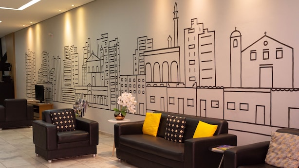 Una hall d'hotel moderna con un murale raffigurante uno skyline urbano, divani in pelle nera e un tavolino con un vaso di fiori.