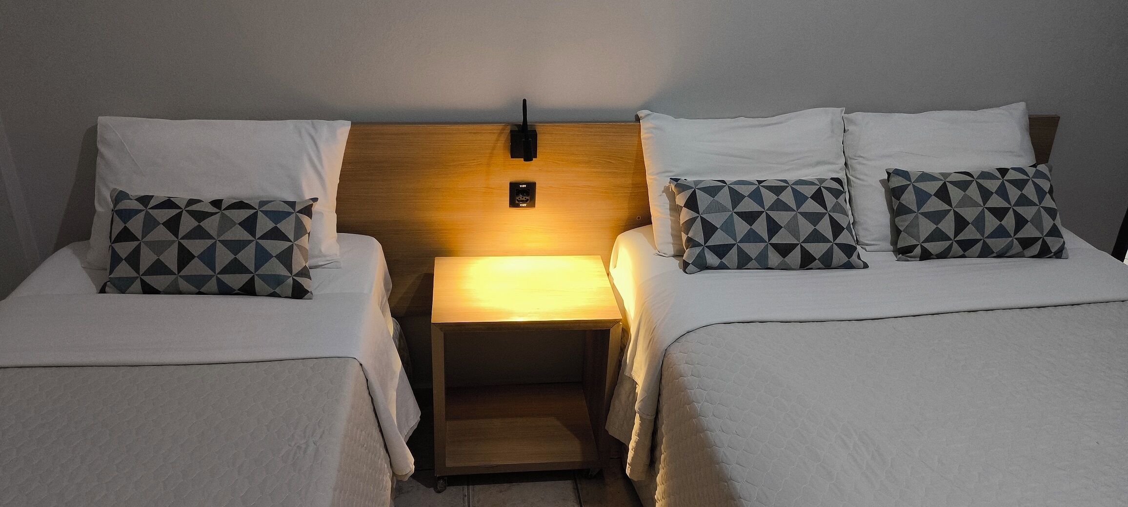 Habitació d'hotel amb dos llits, cadascun amb coixí i una tauleta de nit amb làmpada.